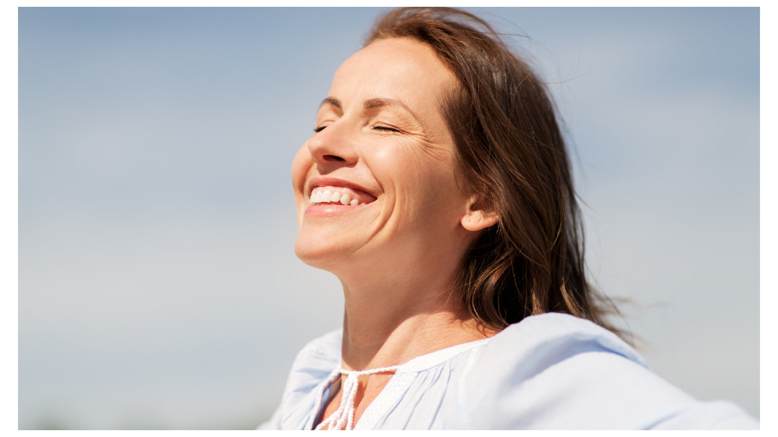 Woman with closed eyes smiling against a clear blue sky